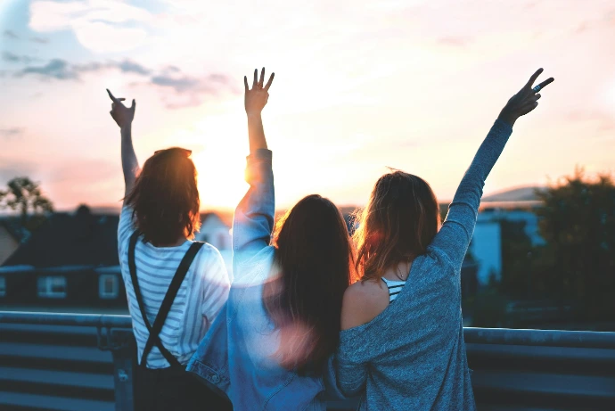 Three people with arms raised against a warm orange sky at low sun